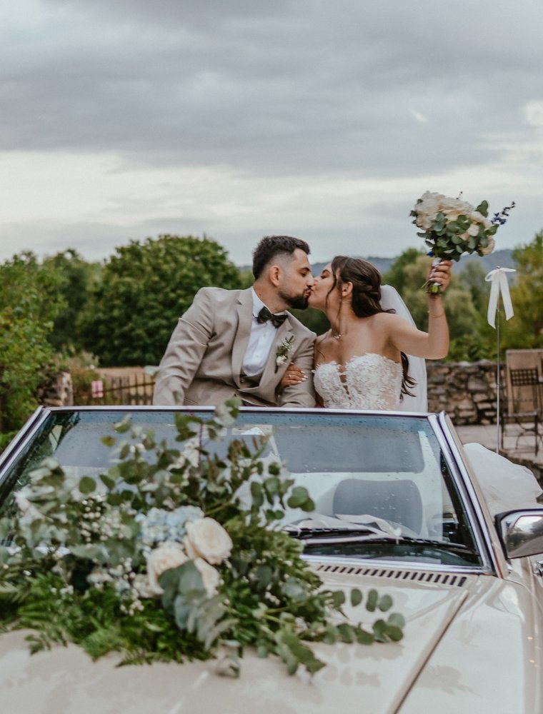 Mariés s’embrassant dans une voiture de collection décorée de fleurs – photographe mariage Alberville
