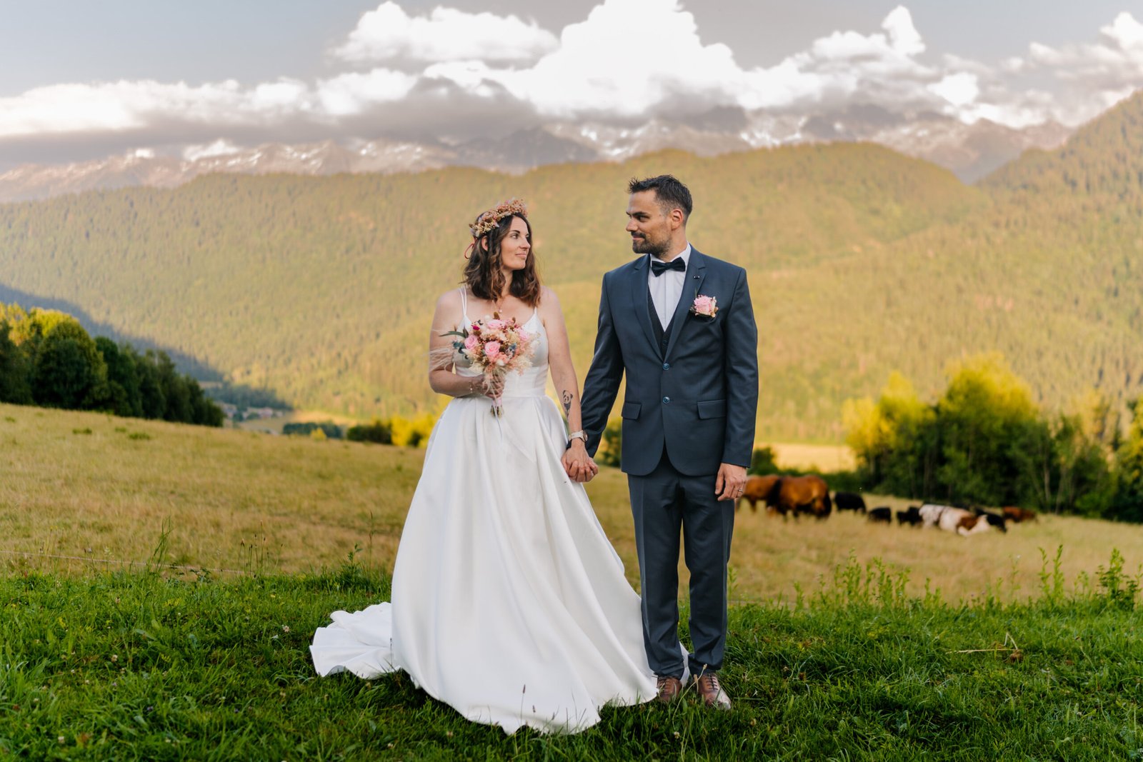 Mariage de Lucie et Cyril en Savoie – couple de mariés posant main dans la main dans un champ face aux montagnes alpines.